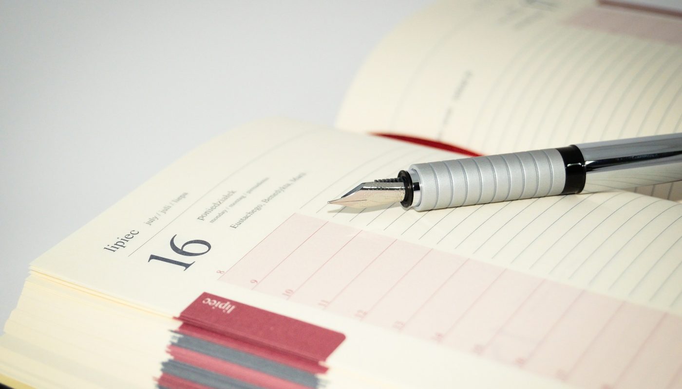 Photo of an opened schedule planner with a fountain pen laying across it
